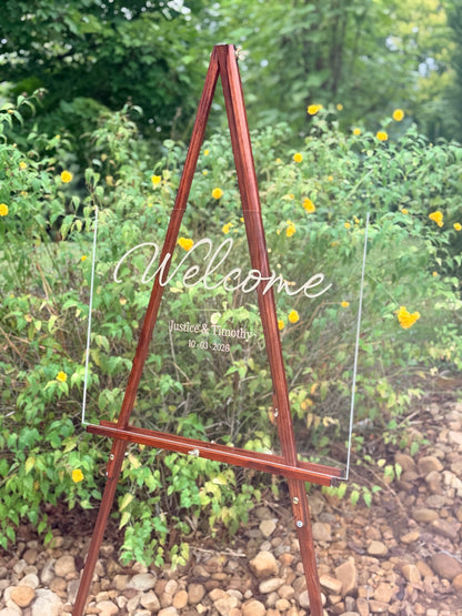 Custom acrylic wedding welcome sign displayed on a wooden easel outdoors
